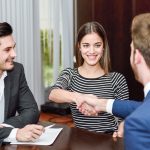 Smiling young couple shaking hands with an insurance agent or investment adviser