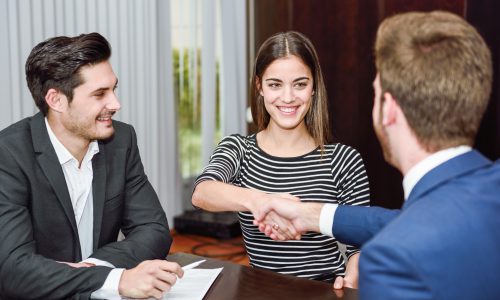 Smiling young couple shaking hands with an insurance agent or investment adviser